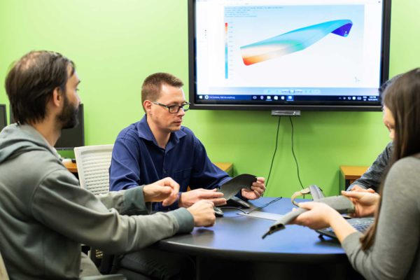 people sitting around a table having a meeting in front of a screen showing a 3d rendering